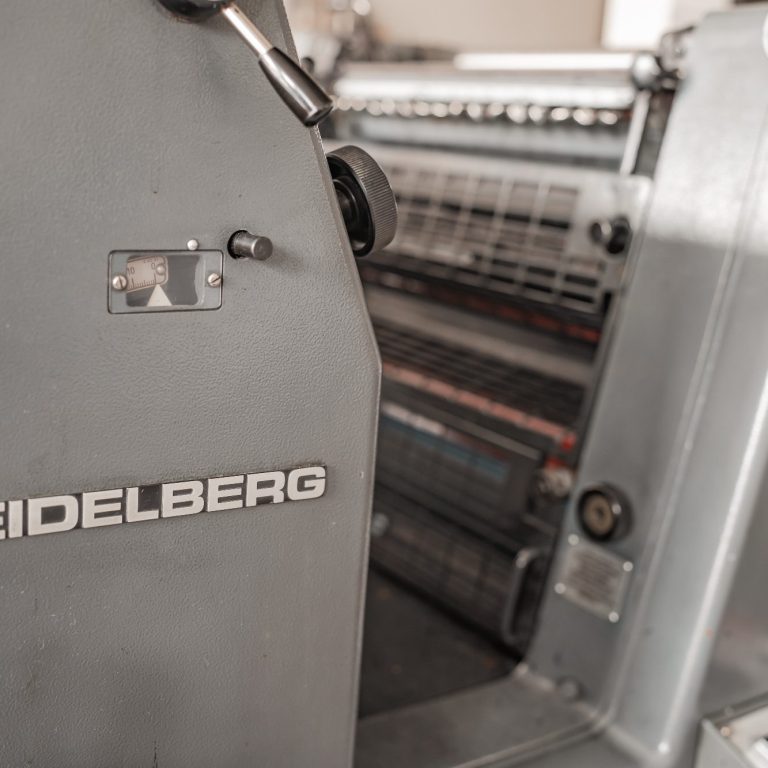 Heidelberg Druckmaschine in einer Druckerei, Fokus auf Bedienfeld und Maschine.